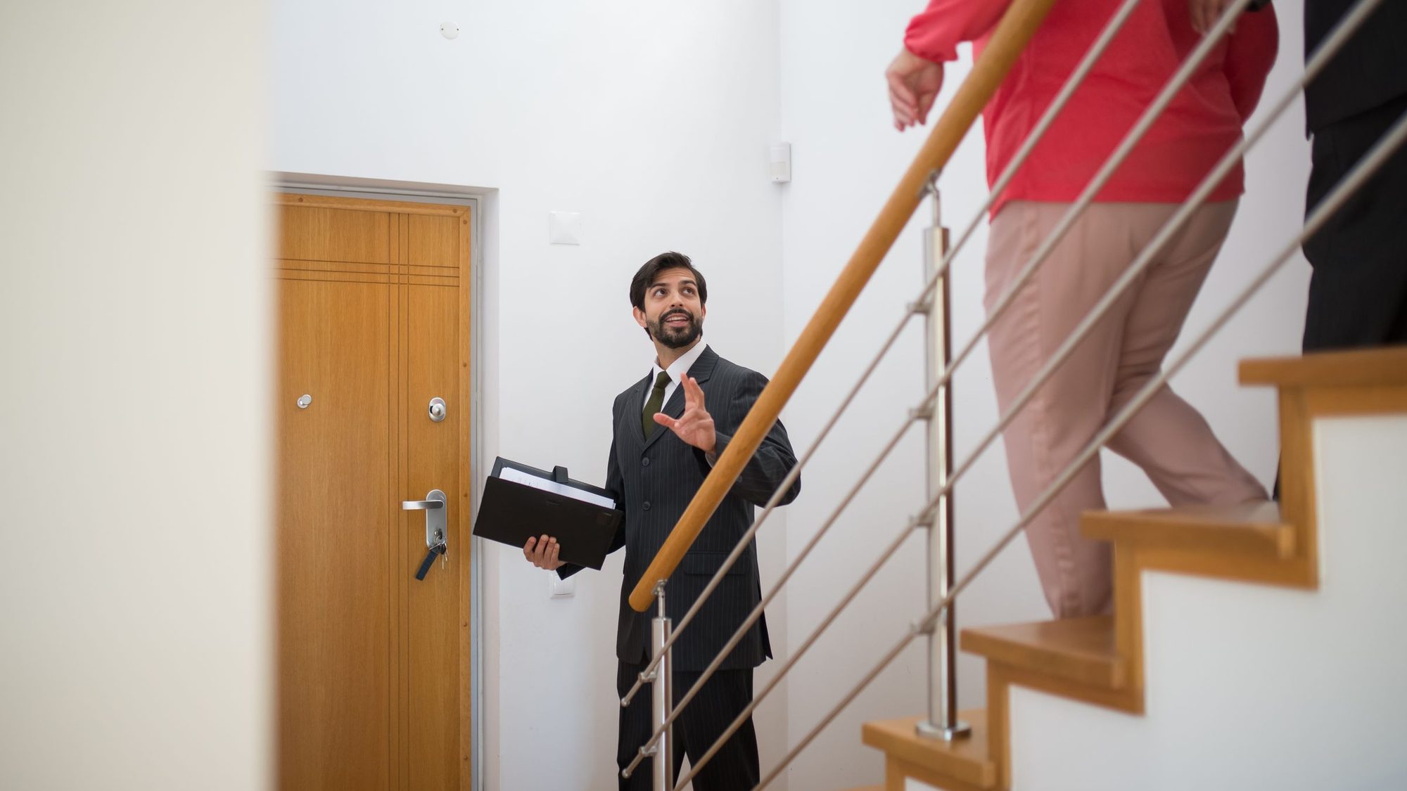 An agent holding a folder shows buyers up a staircase in a house