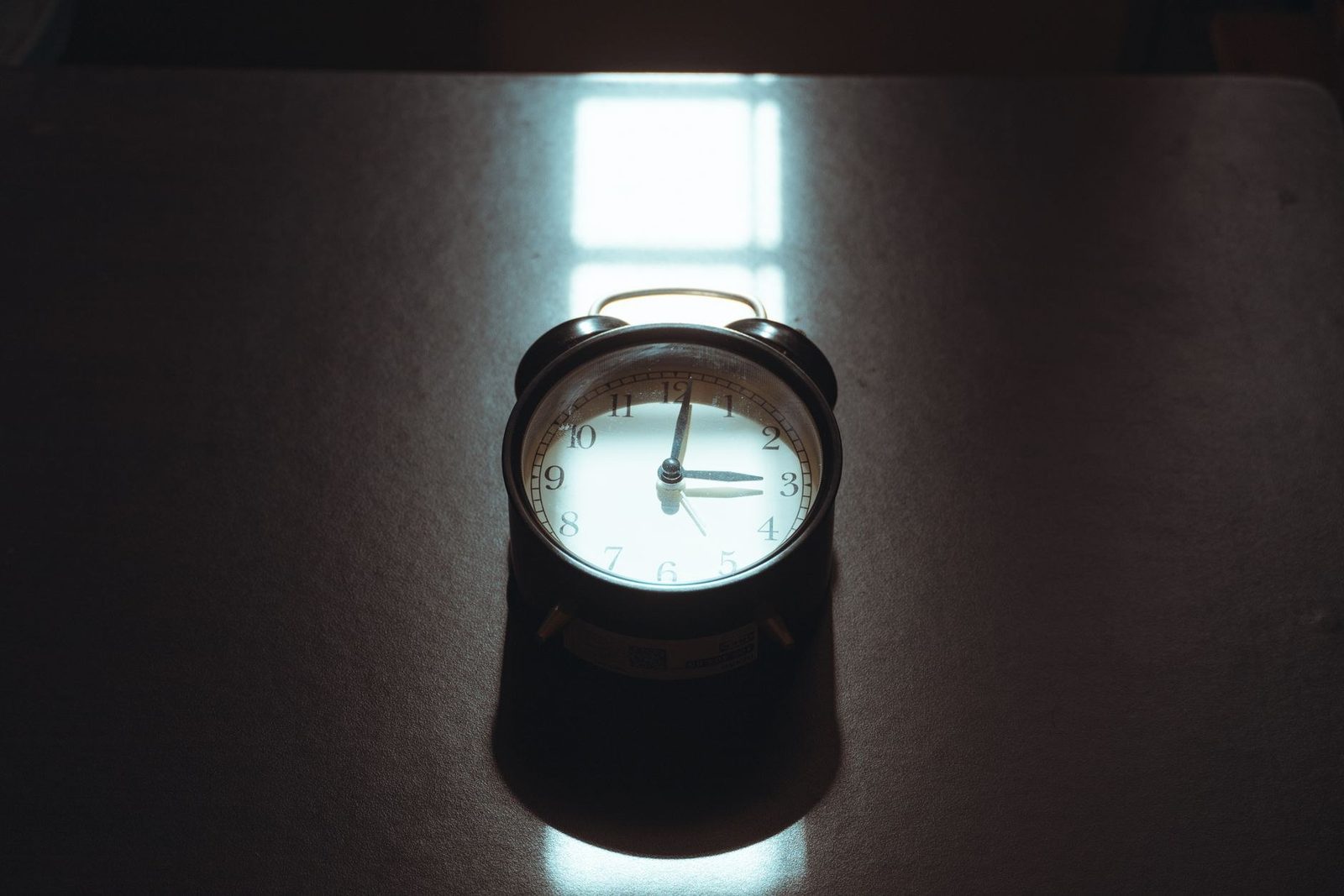 An alarm clock on a dark desk, lit by a window at night