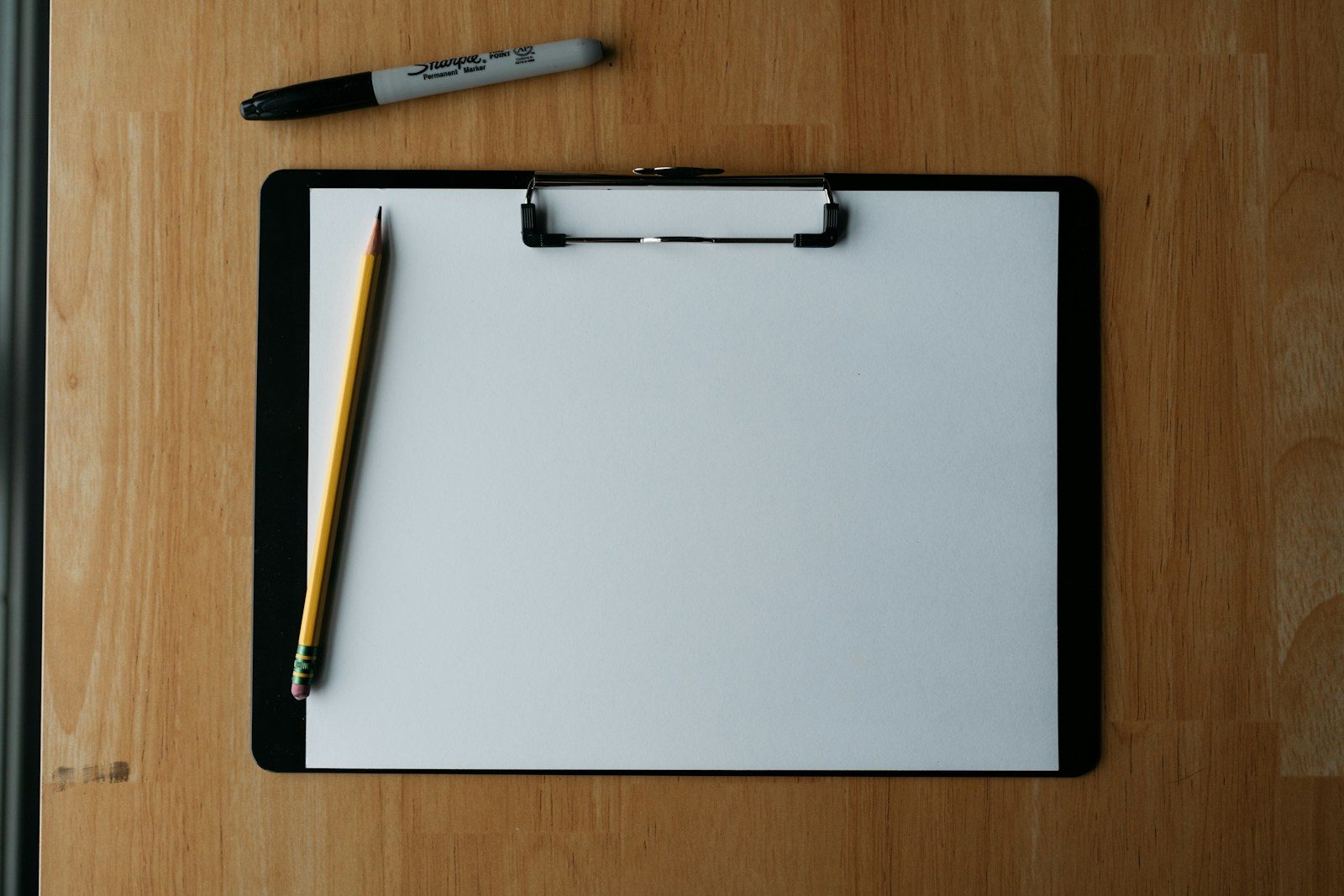 A blank clipboard and a pencil on a wooden table