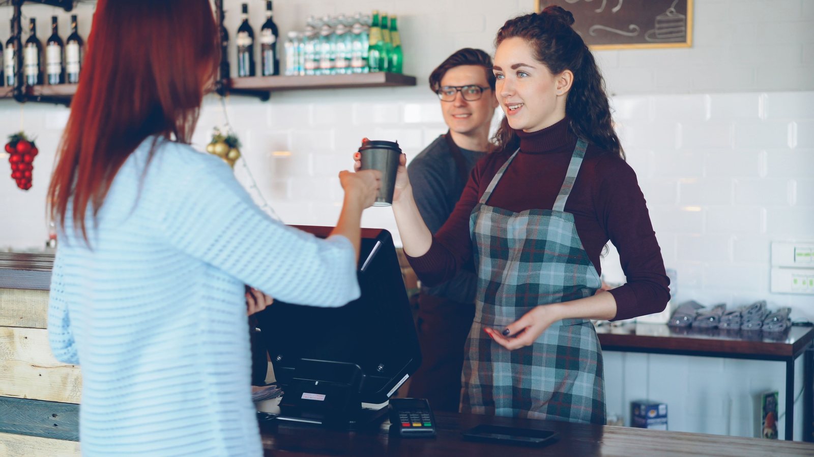A barista handing a coffee across the counter to a customer