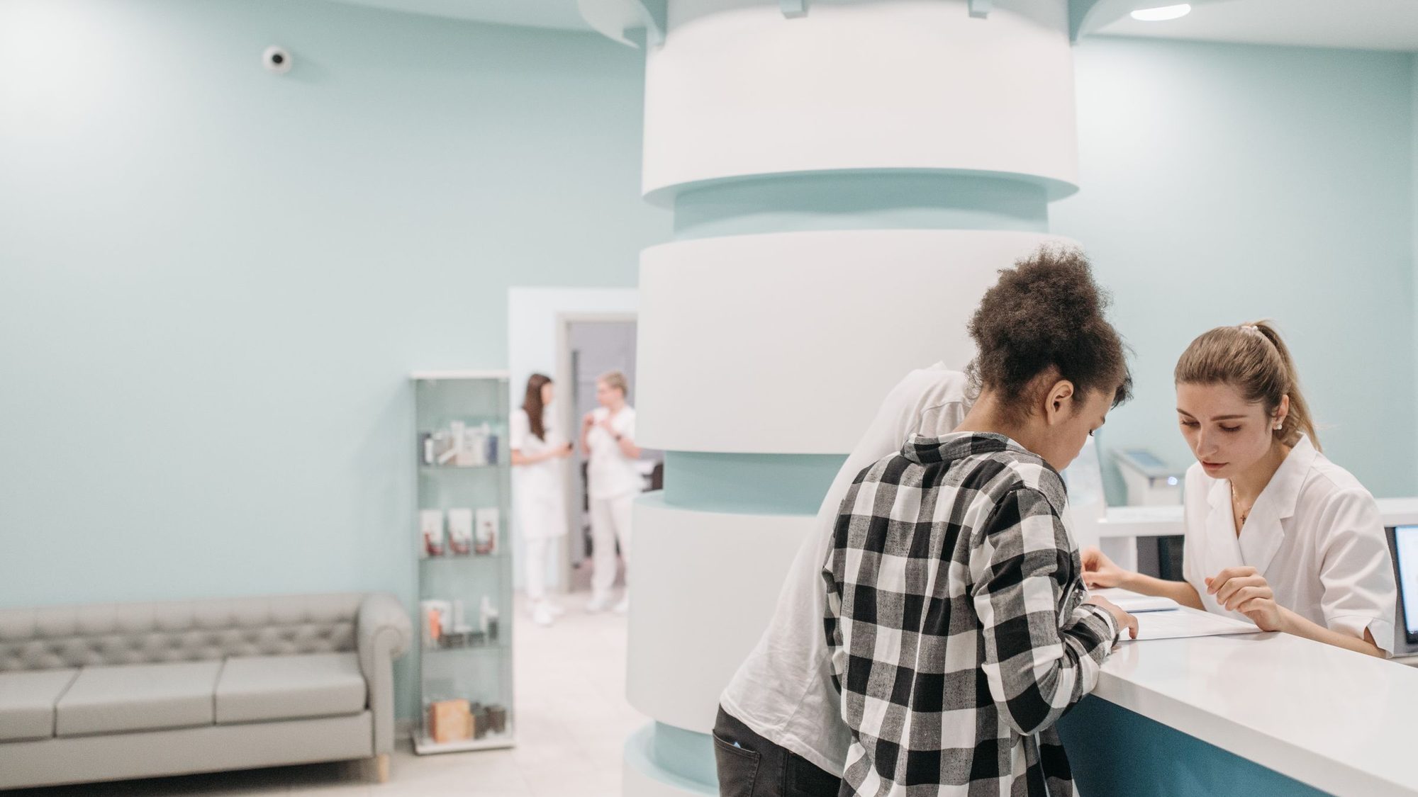 A receptionist helps a visitor at a clinic front desk