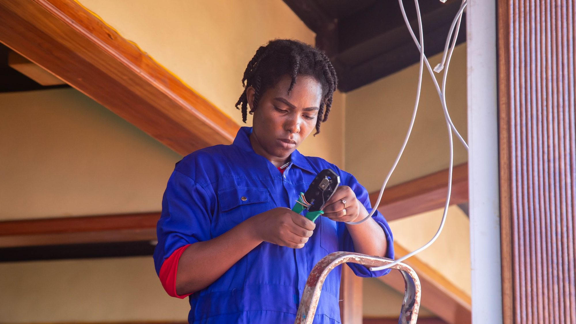 An electrician in blue coveralls works on wiring indoors