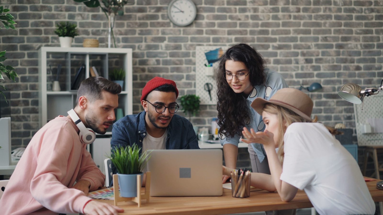 Four coworkers gather around one laptop at a table