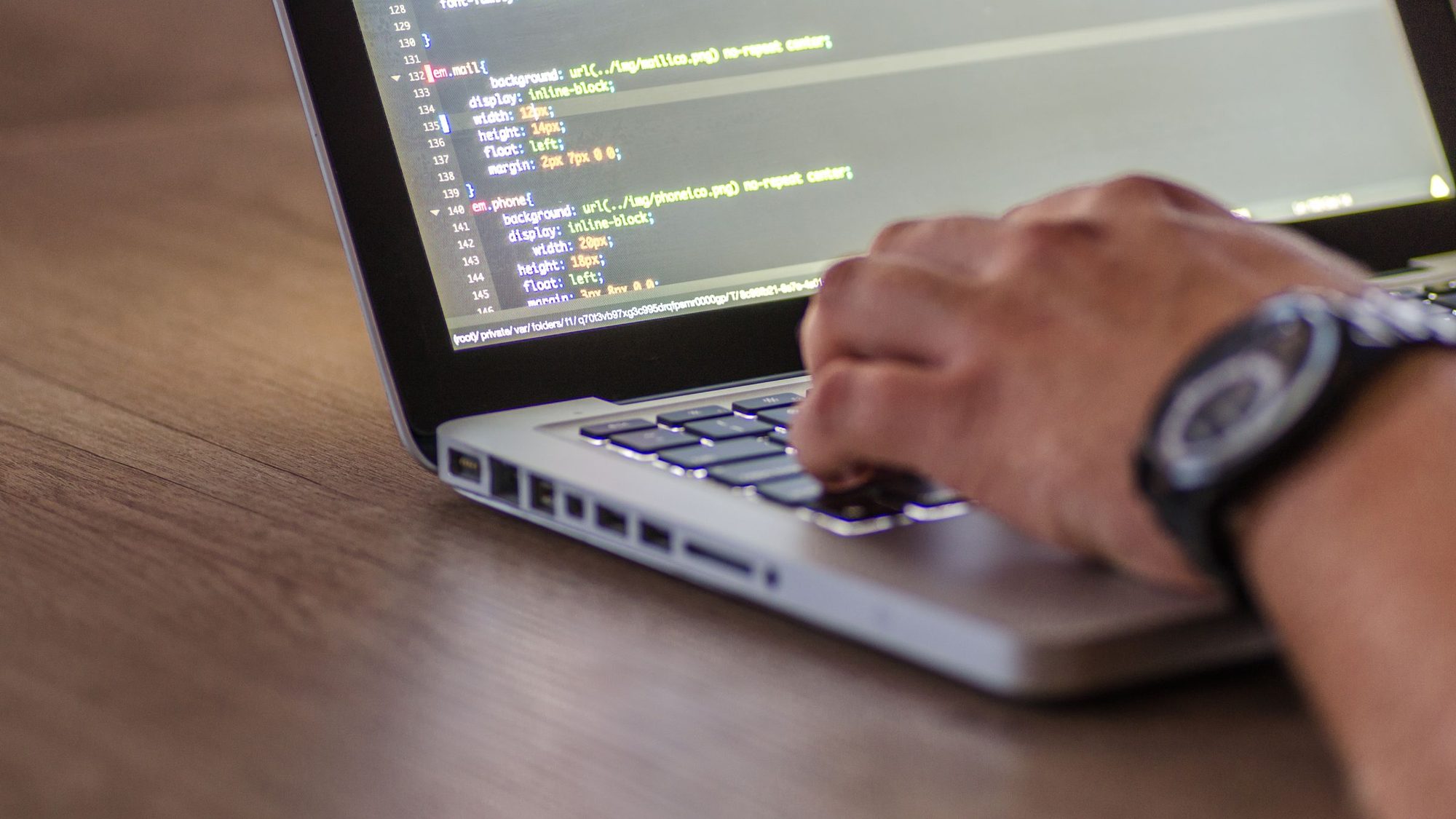 Close up of hands typing on a laptop with code on the screen