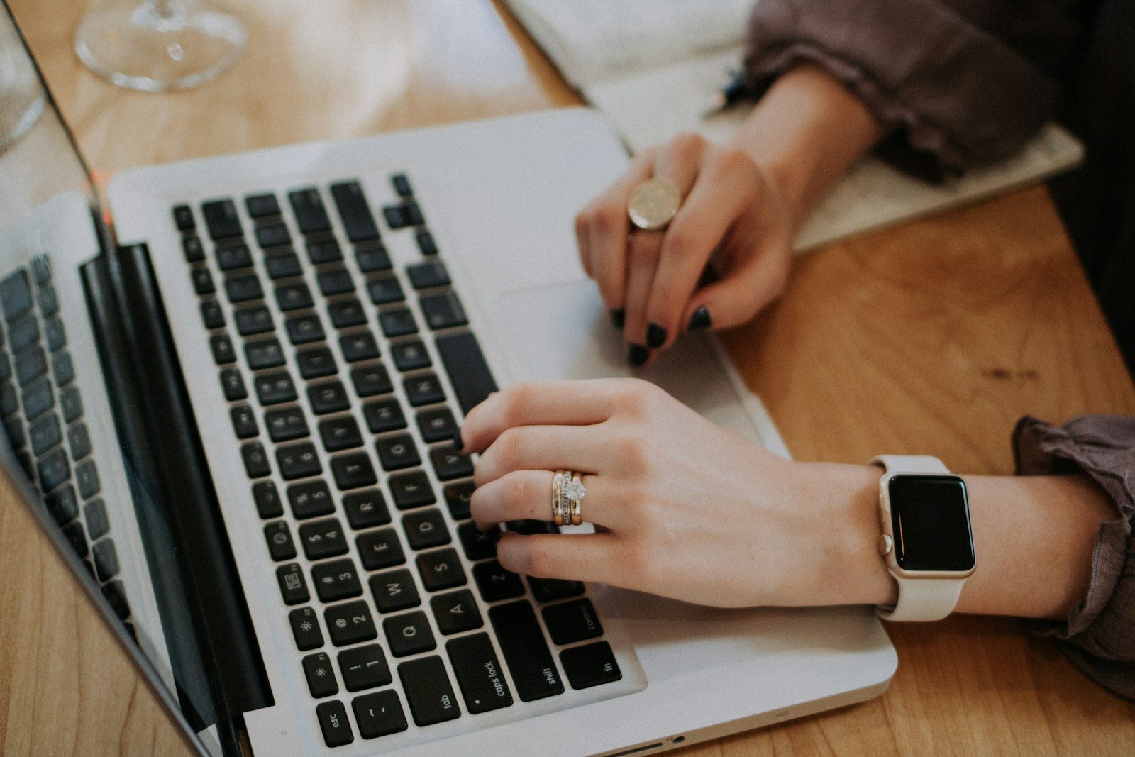 Hands type on a laptop at a wooden table