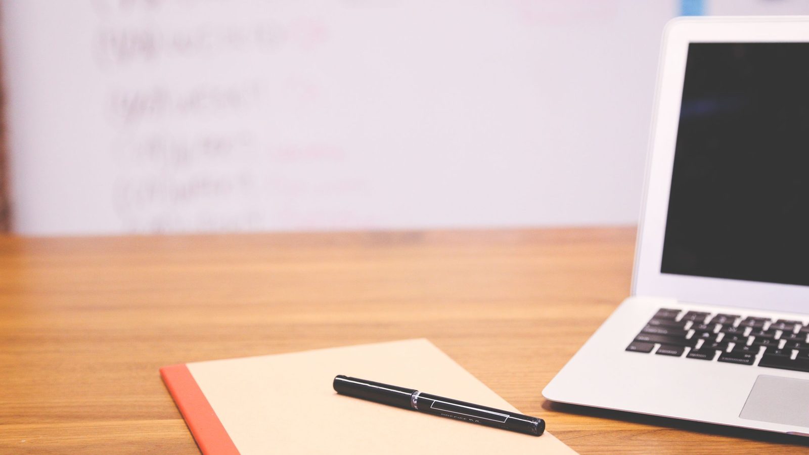 A laptop, a notebook and a pen on a wooden desk