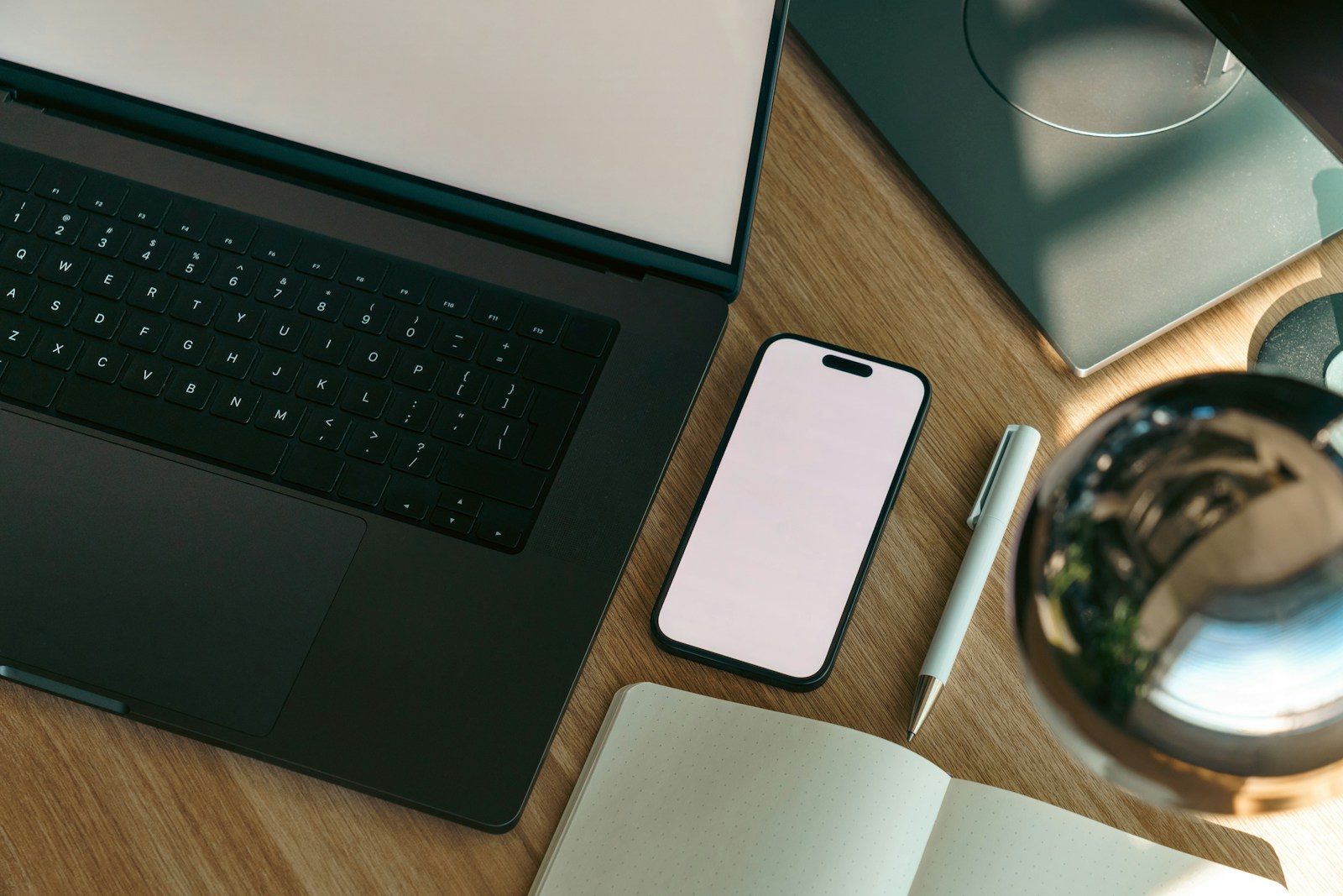 A laptop, a phone and a notebook on a wooden desk