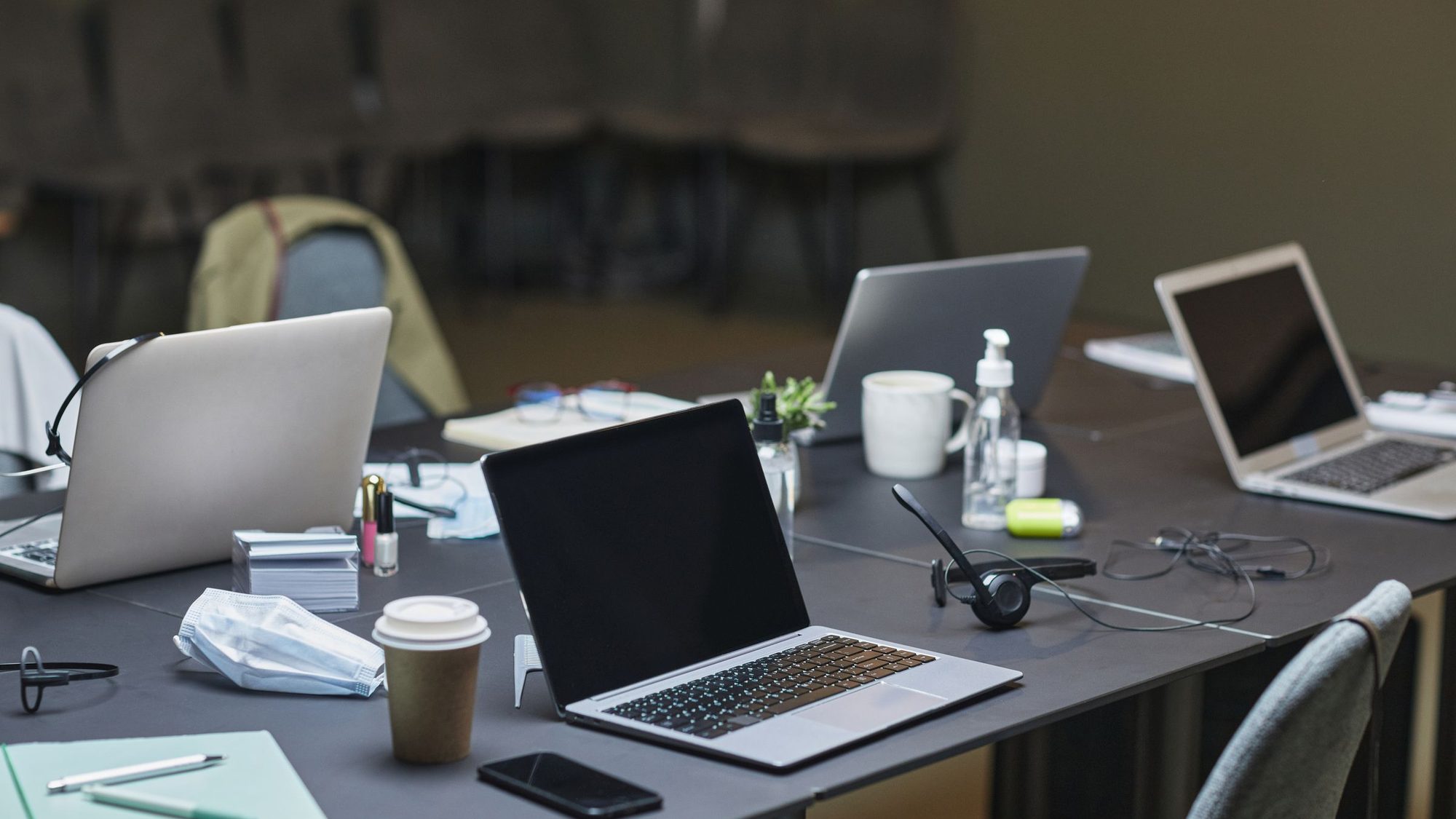 Several laptops, coffee cups and a headset on shared office desks