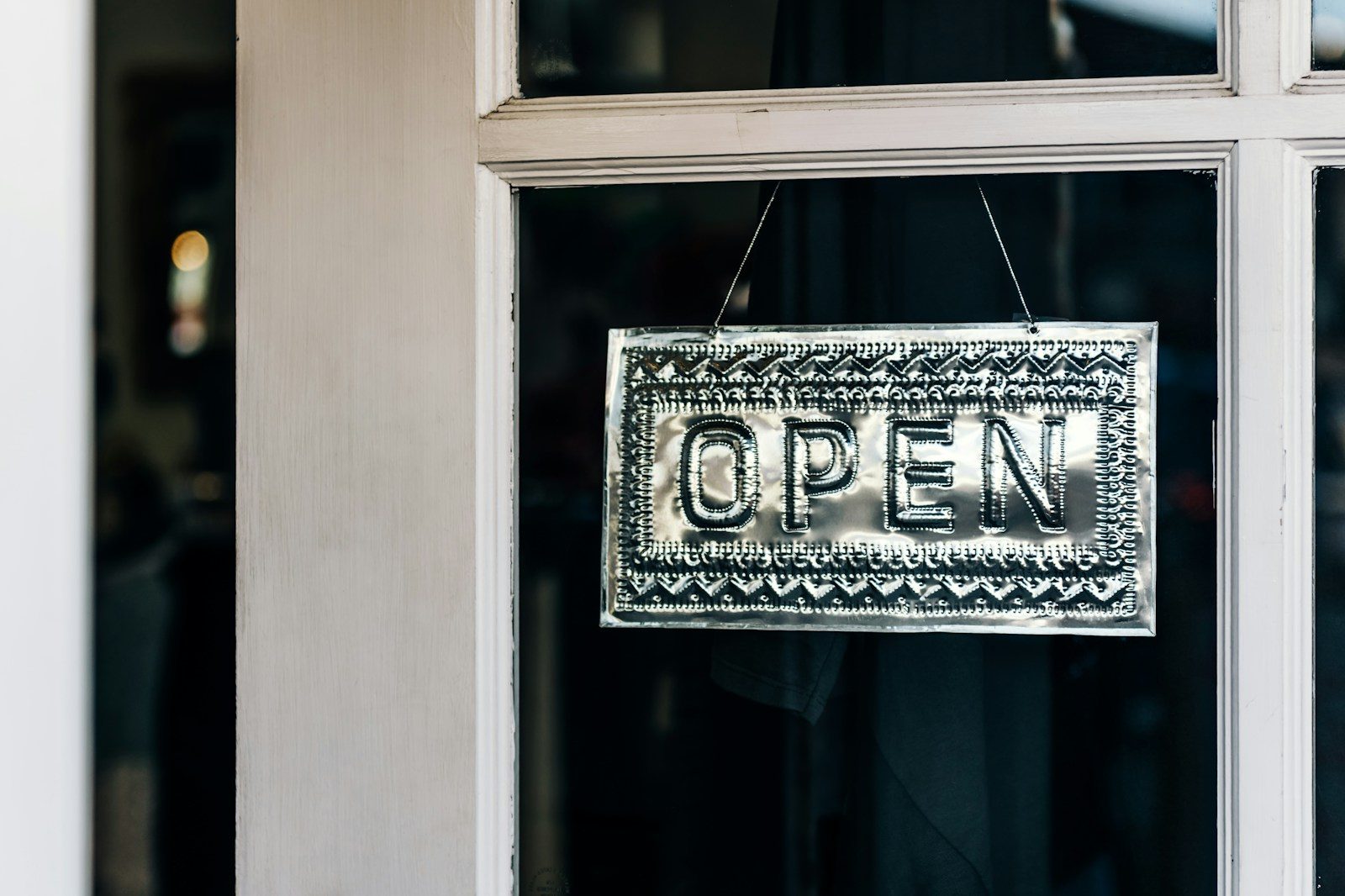 A metal Open sign hangs in the glass door of a shop