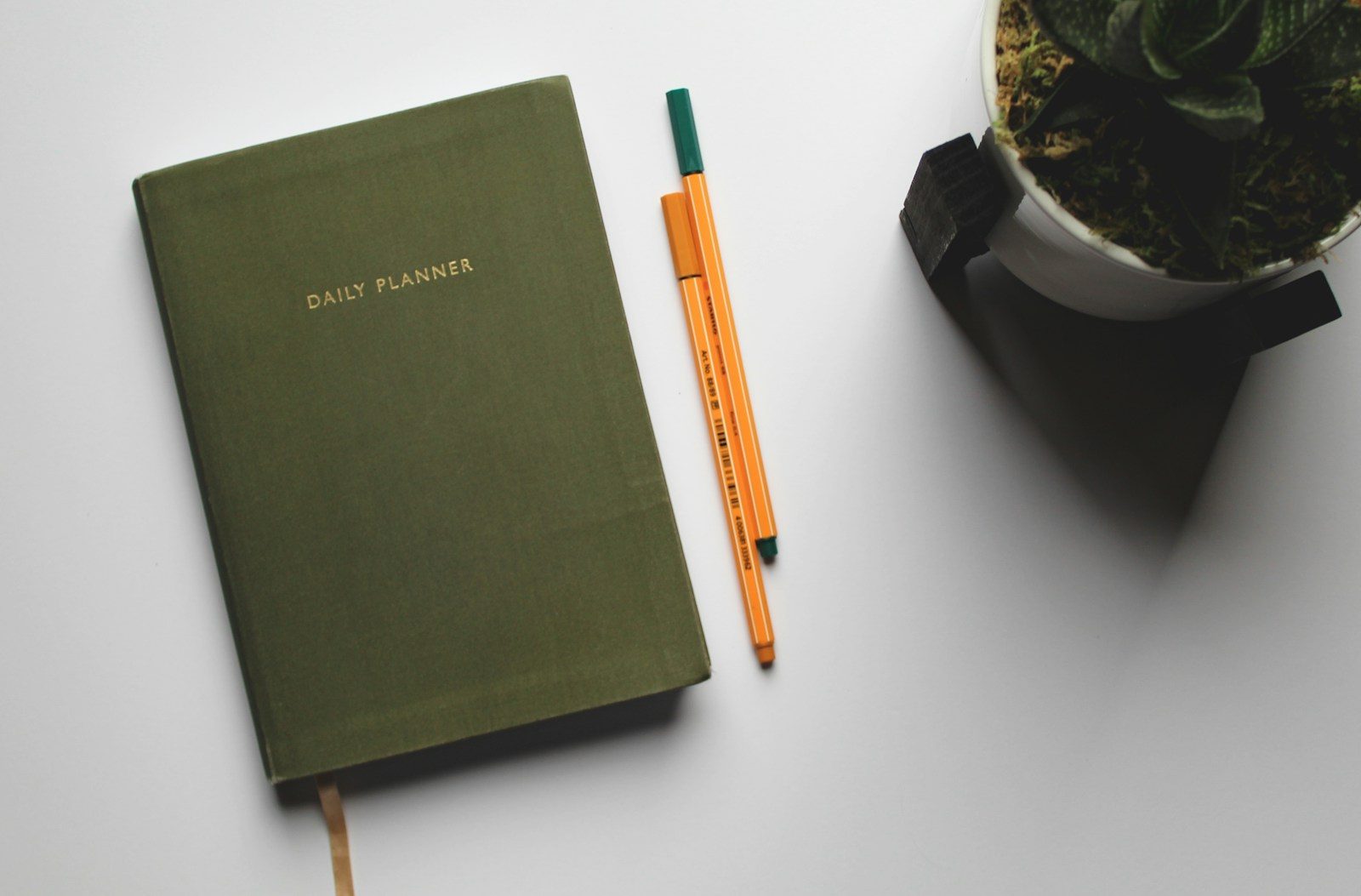 A closed daily planner and an orange pen on a white desk