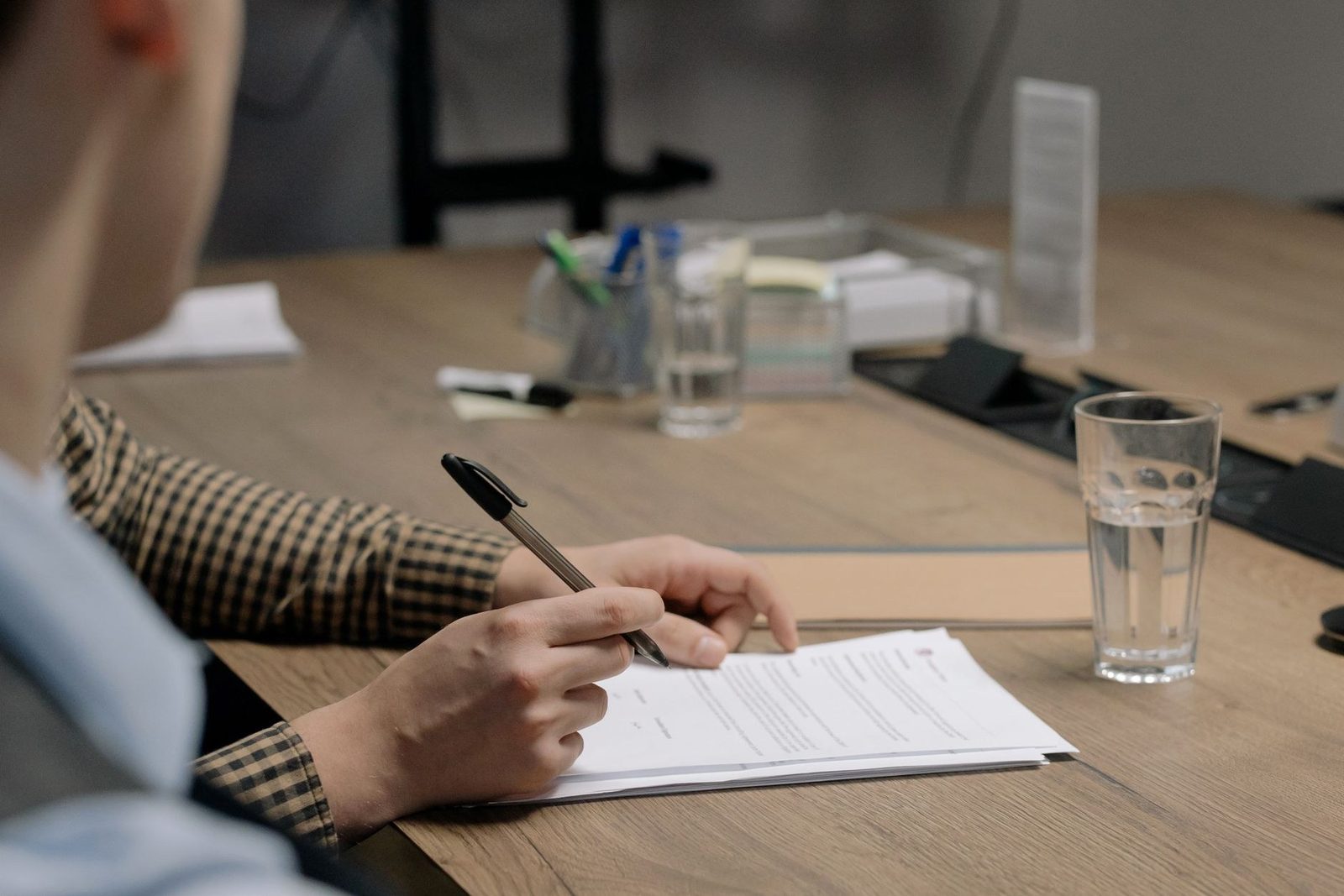 A person signs a document at a wooden table