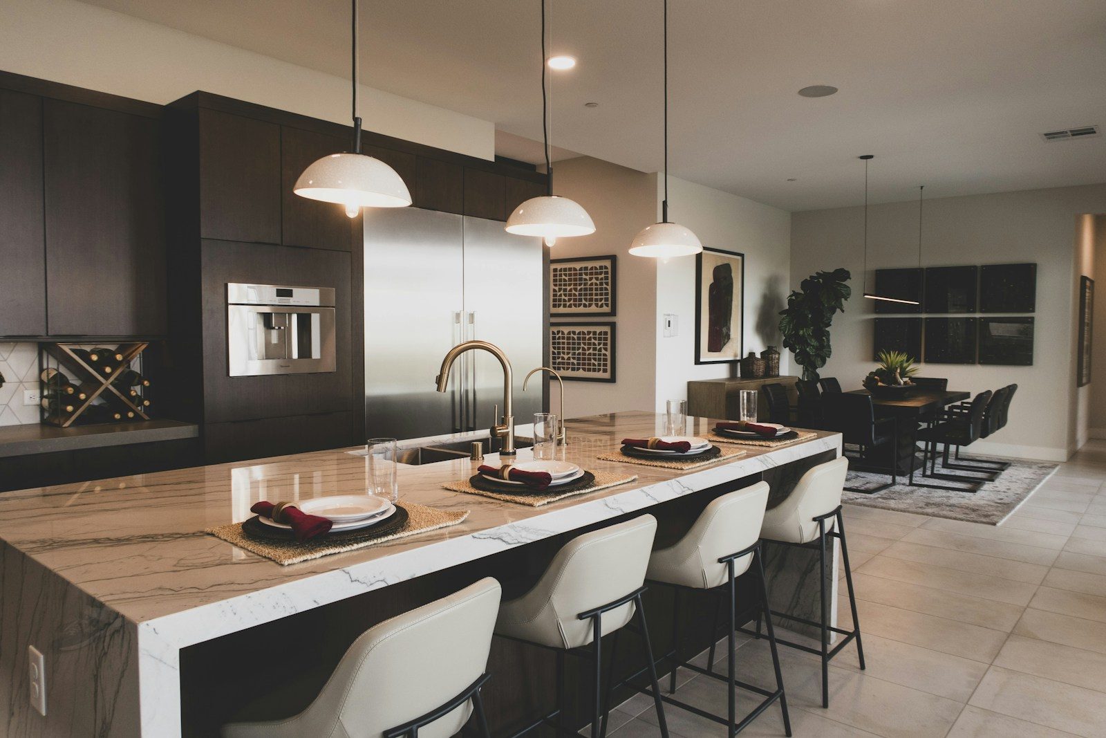 A staged kitchen with a marble island, bar stools and pendant lights