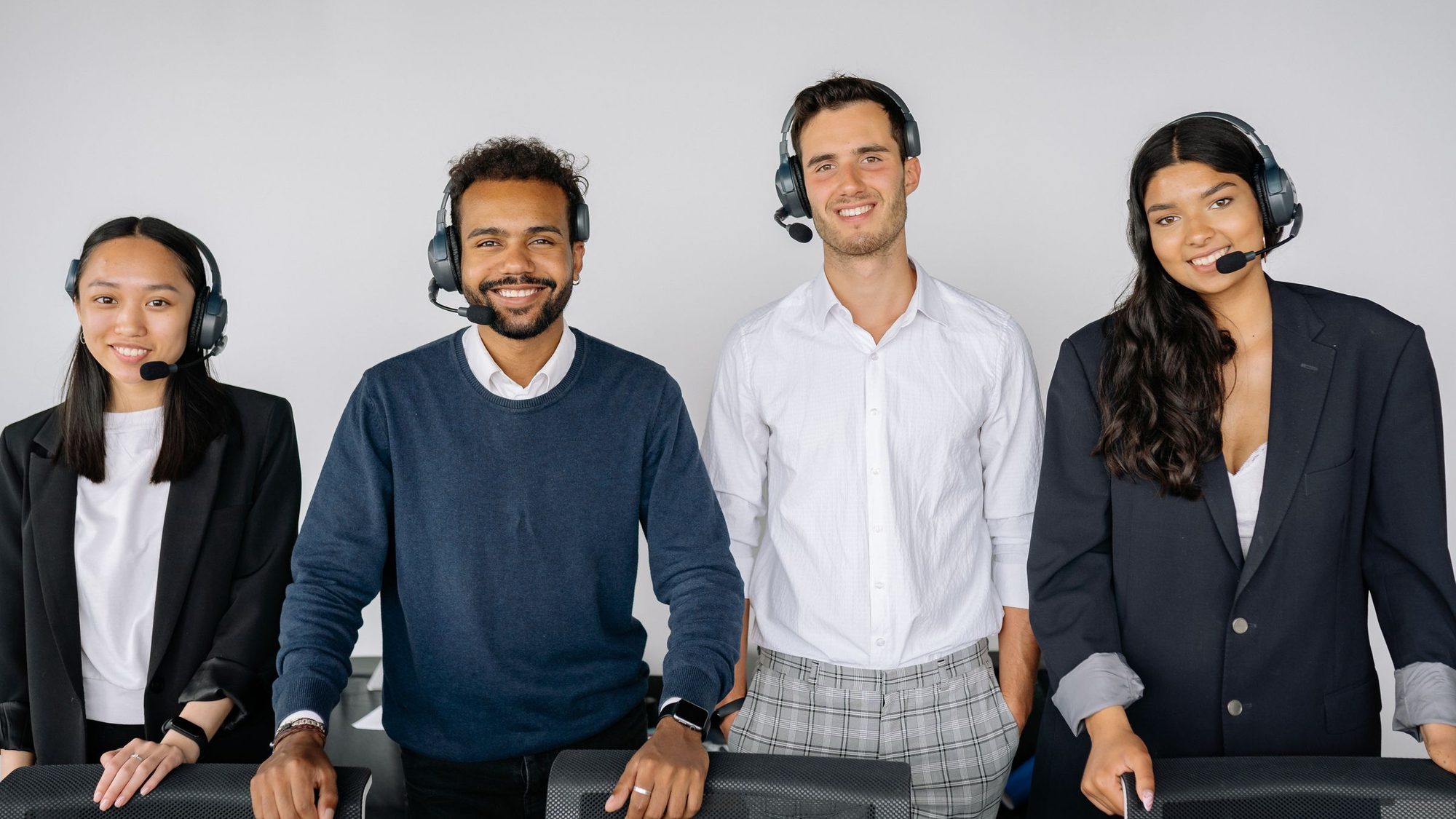 Four customer support staff wearing headsets smile at the camera