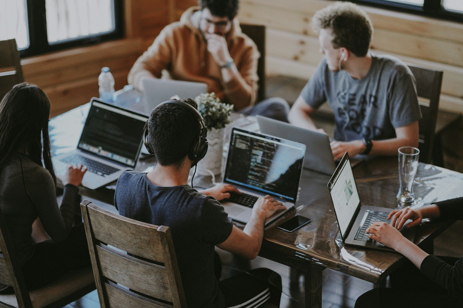 A team works on laptops around a shared wooden table