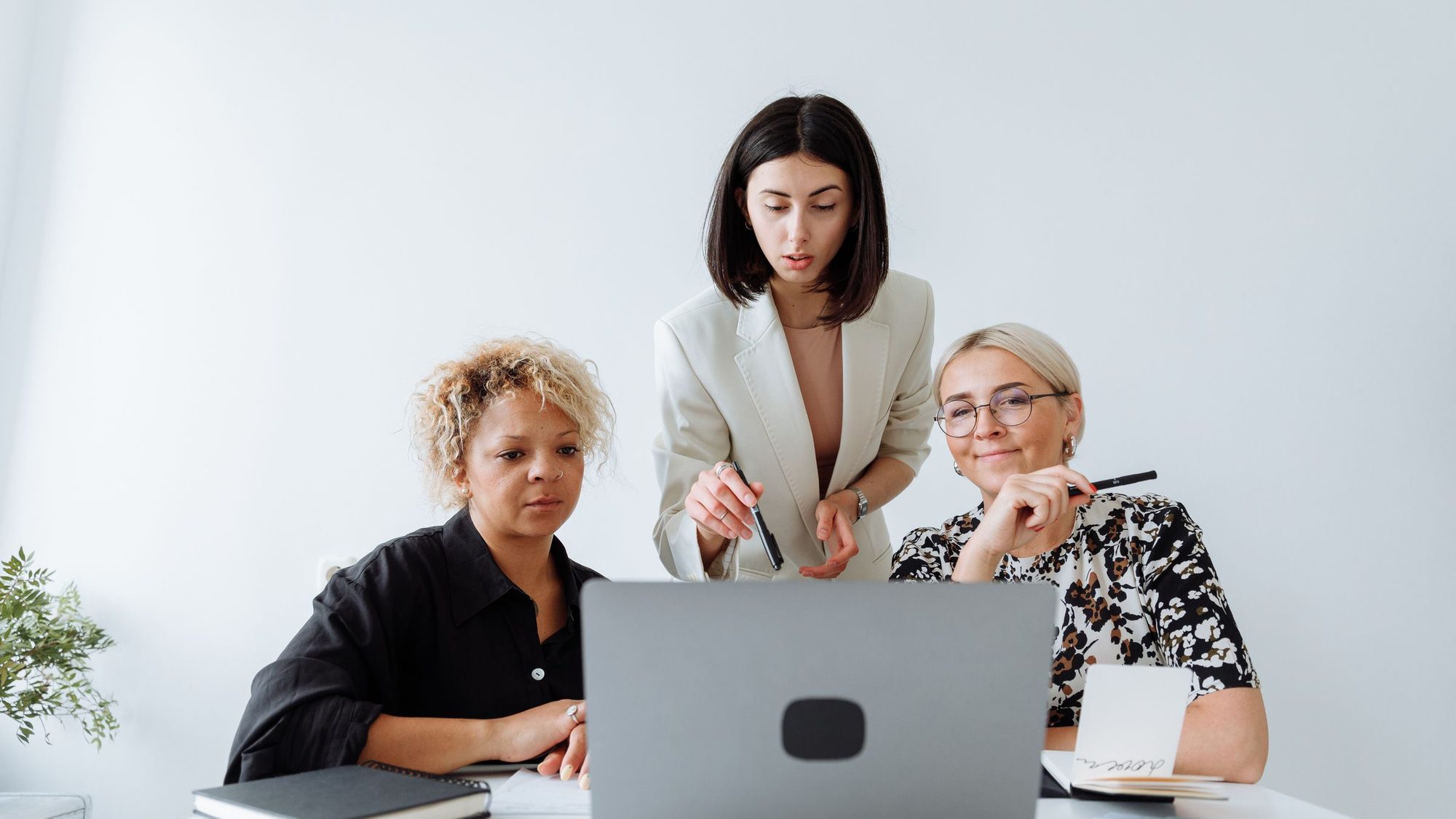 Three women look at a laptop together in a bright office