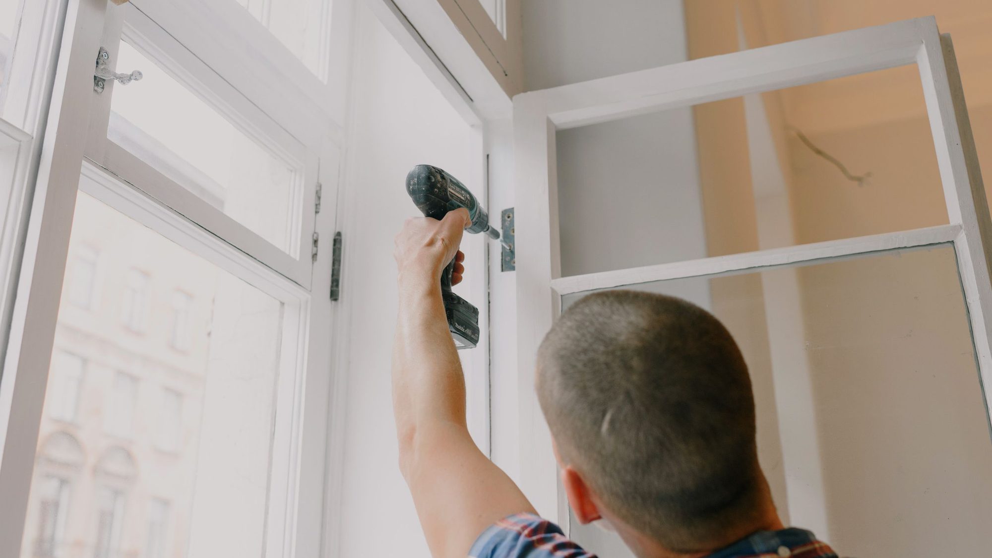 A tradesman uses a cordless drill on a white window frame