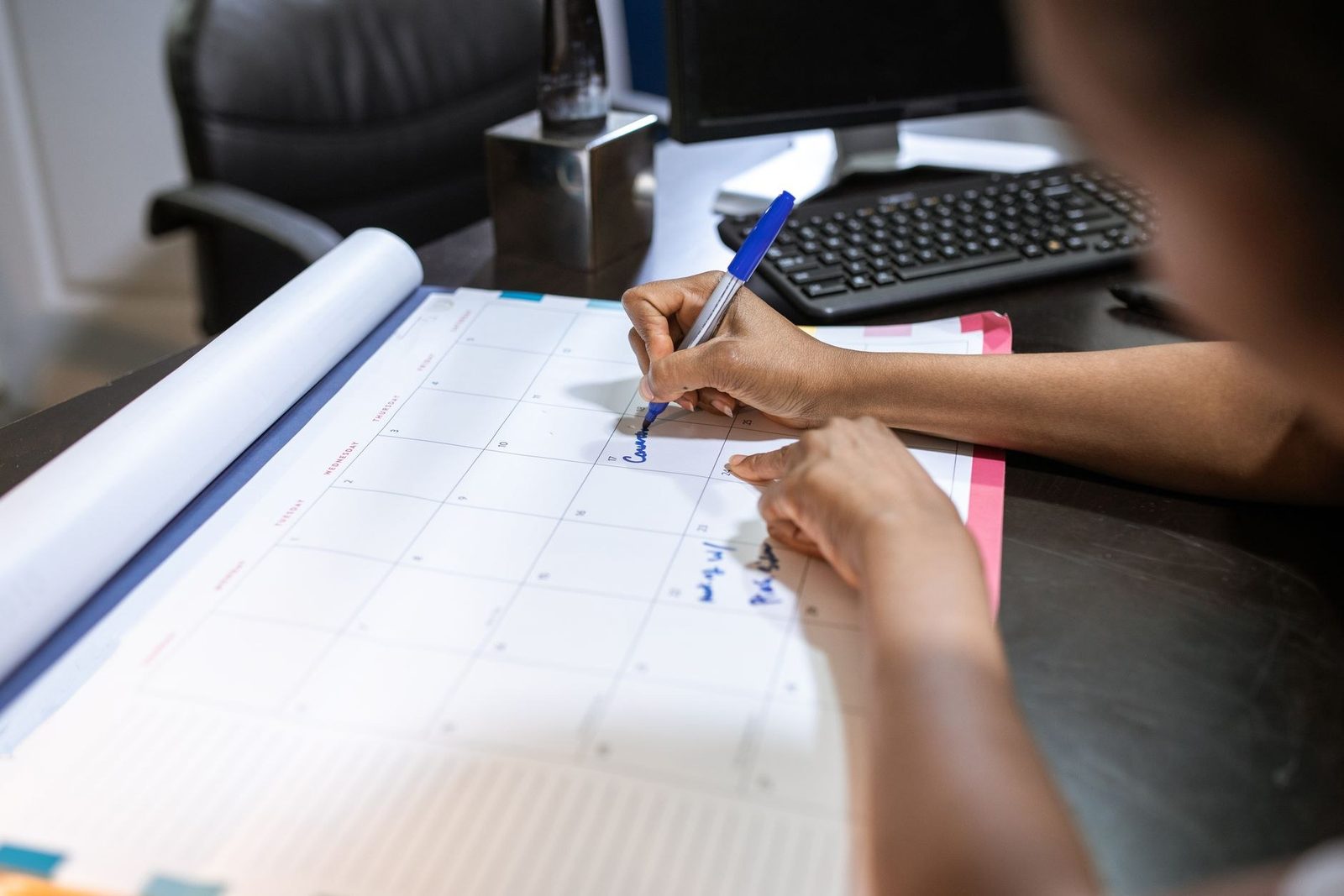 A person writes an appointment on a large desk calendar